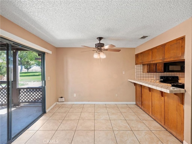 kitchen featuring light tile patterned flooring, tile countertops, decorative backsplash, and black appliances