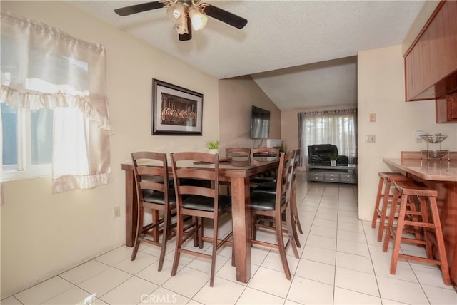 dining room with ceiling fan, a textured ceiling, lofted ceiling, and light tile patterned flooring