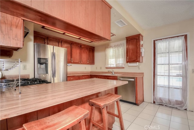 kitchen featuring light tile patterned floors, sink, kitchen peninsula, appliances with stainless steel finishes, and a breakfast bar