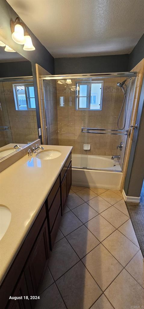 bathroom with tile patterned flooring, vanity, a textured ceiling, and combined bath / shower with glass door