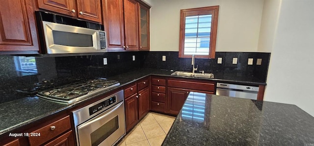 kitchen with sink, dark stone counters, decorative backsplash, light tile patterned floors, and appliances with stainless steel finishes