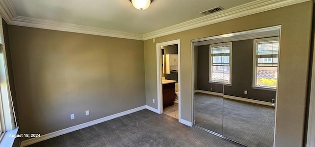 unfurnished bedroom with dark colored carpet, ornamental molding, and connected bathroom