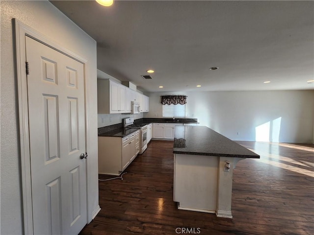 kitchen featuring a breakfast bar, a center island, gas stove, dark hardwood / wood-style flooring, and white cabinetry