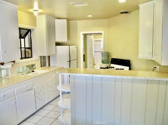 kitchen with stove, light tile patterned floors, white cabinetry, and sink