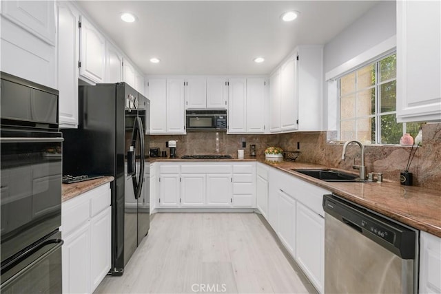 kitchen featuring decorative backsplash, light wood-type flooring, sink, black appliances, and white cabinets