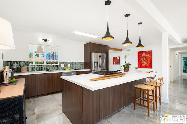 kitchen featuring decorative backsplash, hanging light fixtures, dark brown cabinets, stainless steel appliances, and kitchen peninsula