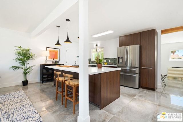 kitchen with a wealth of natural light, stainless steel refrigerator with ice dispenser, decorative light fixtures, and backsplash