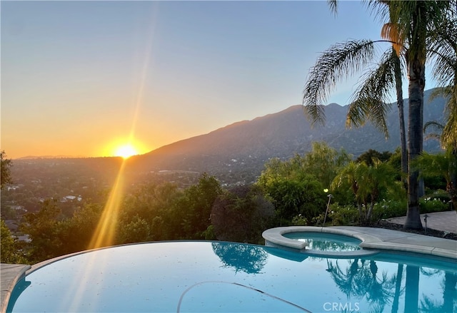 pool at dusk featuring an in ground hot tub and a mountain view