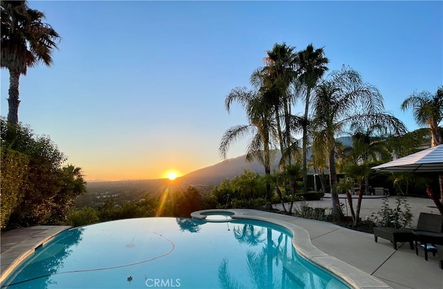 pool at dusk with an in ground hot tub, a patio area, and a mountain view