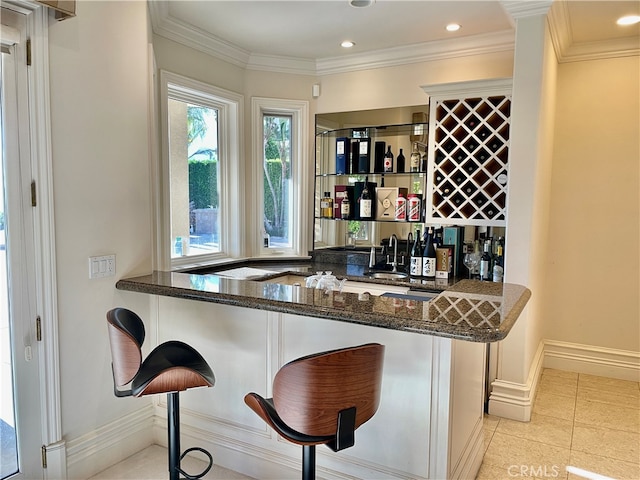 bar featuring crown molding, dark stone countertops, sink, and light tile patterned floors