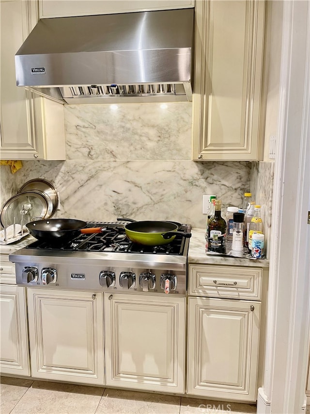 kitchen with cream cabinets, backsplash, stainless steel gas stovetop, light tile patterned flooring, and wall chimney exhaust hood