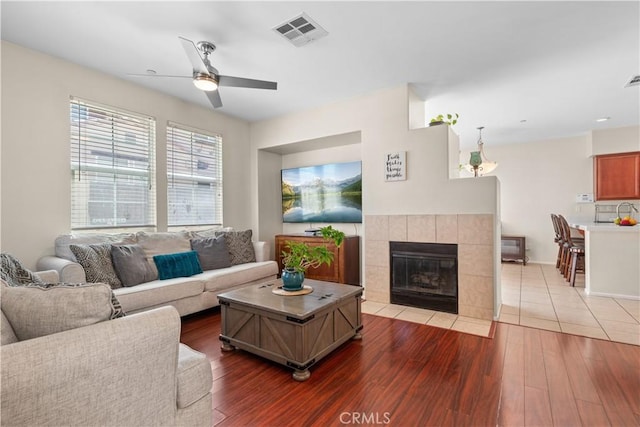 living room featuring a tile fireplace, ceiling fan, and wood-type flooring