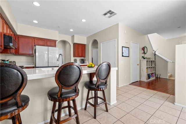 kitchen featuring a kitchen breakfast bar, tile countertops, white fridge, and light tile patterned floors