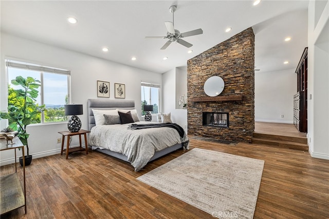 bedroom with ceiling fan, a stone fireplace, dark wood-type flooring, and high vaulted ceiling