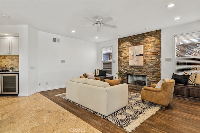 living room with a stone fireplace, ceiling fan, wine cooler, and plenty of natural light