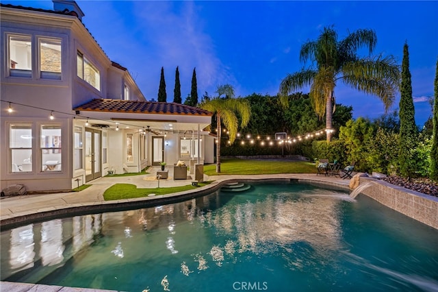 pool at dusk with ceiling fan, a lawn, and a patio