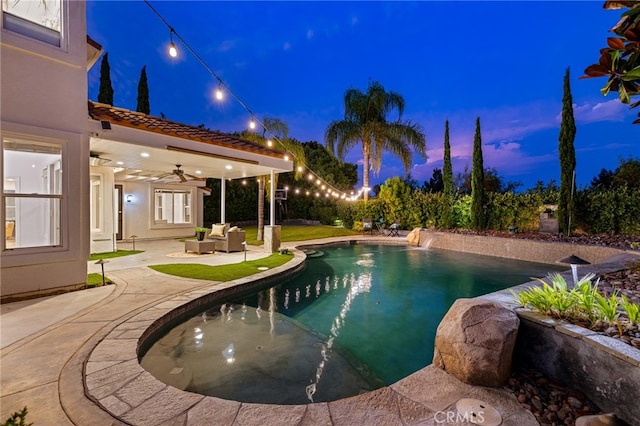 pool at dusk featuring ceiling fan, pool water feature, and a patio area