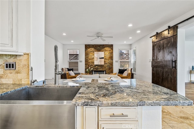 kitchen featuring light stone counters, white cabinets, tasteful backsplash, a stone fireplace, and a barn door