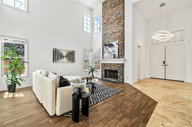 living room featuring a towering ceiling, a chandelier, plenty of natural light, and a stone fireplace