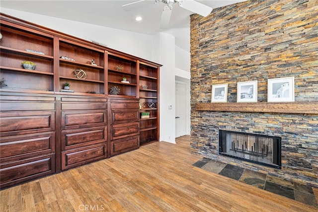 unfurnished living room featuring light hardwood / wood-style flooring, lofted ceiling, ceiling fan, and a stone fireplace