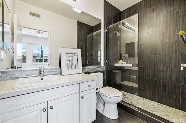 bathroom with tile walls, walk in shower, ceiling fan, vanity, and toilet