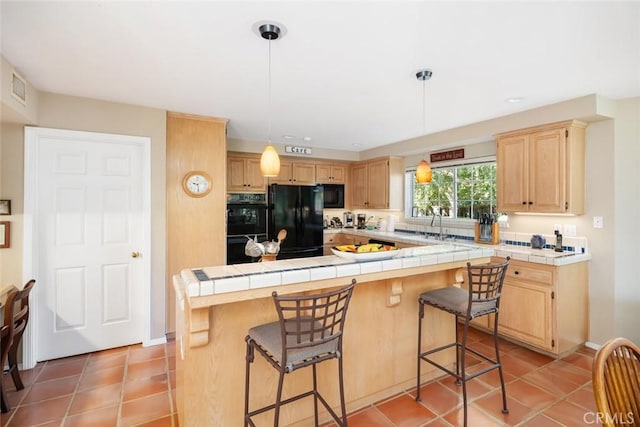 kitchen with light brown cabinetry, black appliances, tile countertops, a center island, and hanging light fixtures