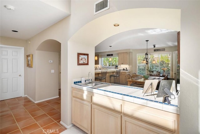 kitchen featuring tile countertops, sink, light tile patterned floors, light brown cabinetry, and decorative light fixtures