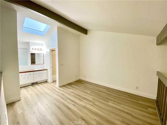 unfurnished bedroom with vaulted ceiling with skylight, ensuite bath, light wood-type flooring, and sink