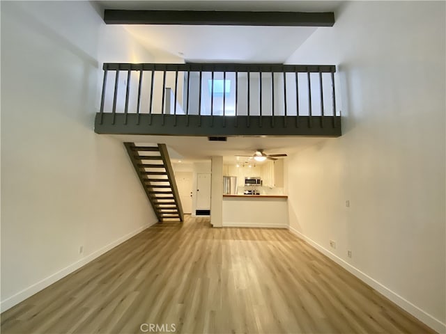 unfurnished living room with light hardwood / wood-style flooring, vaulted ceiling with beams, and ceiling fan