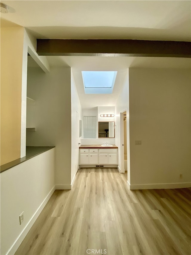 hallway with light wood-type flooring, a skylight, beamed ceiling, and sink