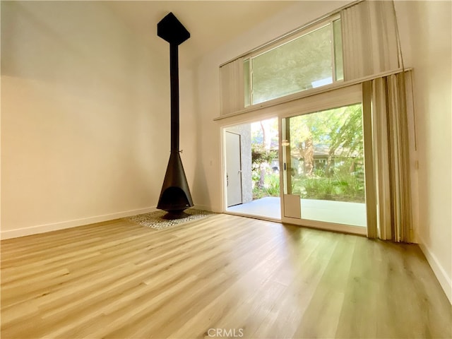 unfurnished living room featuring light hardwood / wood-style floors, a wood stove, and a high ceiling