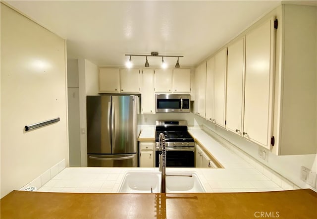 kitchen with appliances with stainless steel finishes, tile countertops, sink, and kitchen peninsula