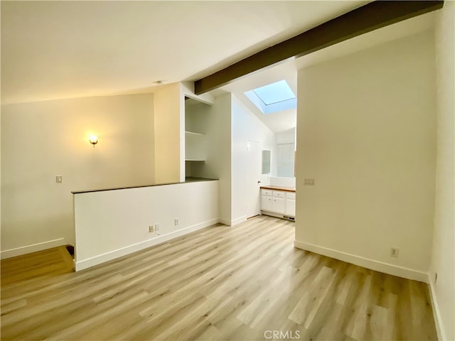 empty room with vaulted ceiling with skylight and light hardwood / wood-style flooring