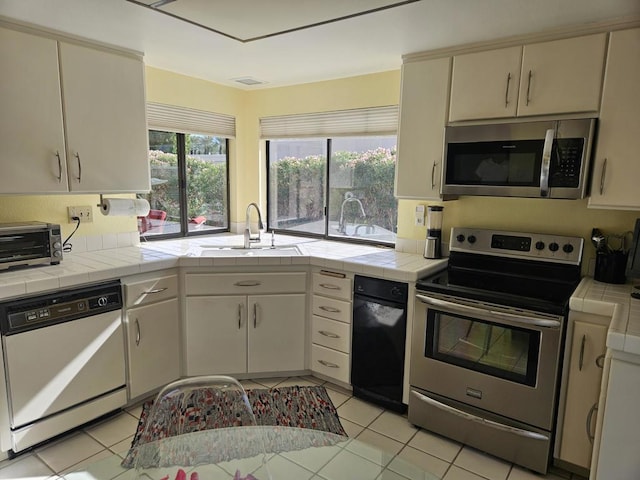 kitchen with sink, light tile patterned floors, tile counters, and appliances with stainless steel finishes