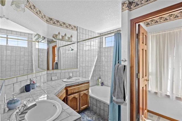 bathroom featuring vanity, a textured ceiling, and tiled shower / bath