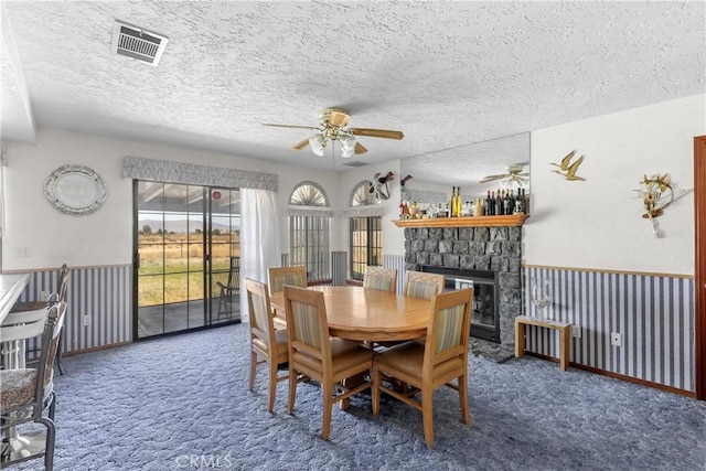 carpeted dining room with ceiling fan, a stone fireplace, and a textured ceiling