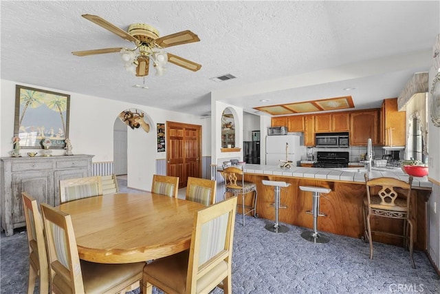 carpeted dining area with ceiling fan and a textured ceiling