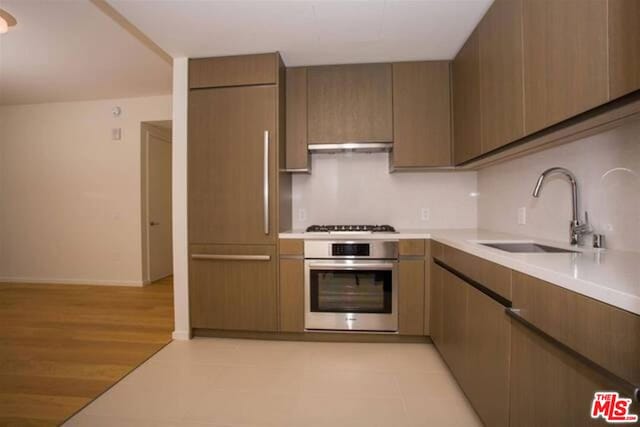 kitchen with sink, stainless steel oven, light hardwood / wood-style floors, paneled built in fridge, and gas cooktop