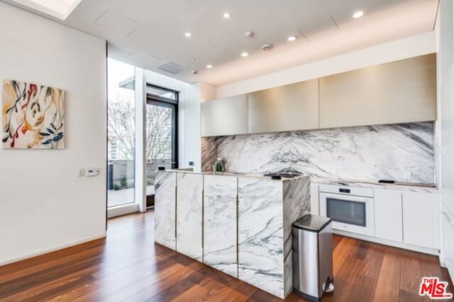 kitchen with dark wood-type flooring, white oven, decorative backsplash, and white cabinets