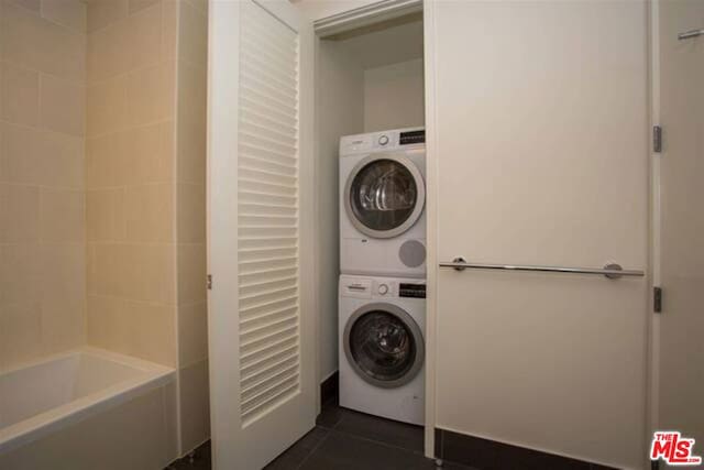 laundry area with stacked washer / drying machine and dark tile patterned flooring