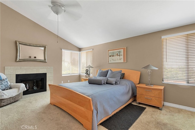 carpeted bedroom with vaulted ceiling, a tiled fireplace, and ceiling fan