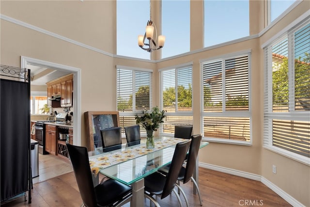 dining space with an inviting chandelier, light wood-type flooring, a high ceiling, and a wealth of natural light