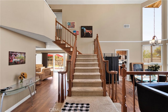 staircase featuring a high ceiling, hardwood / wood-style floors, a chandelier, and a wealth of natural light