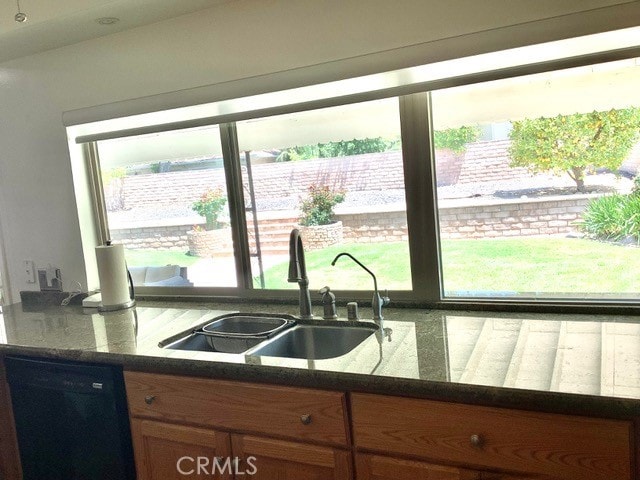 kitchen with dark stone counters, dishwasher, plenty of natural light, and sink