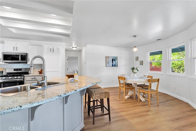 kitchen featuring white cabinetry, light hardwood / wood-style flooring, pendant lighting, a breakfast bar area, and appliances with stainless steel finishes