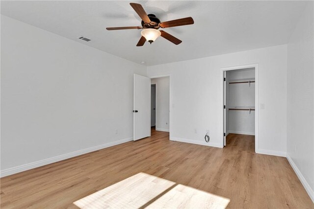 unfurnished bedroom with ceiling fan, a closet, a spacious closet, and light wood-type flooring