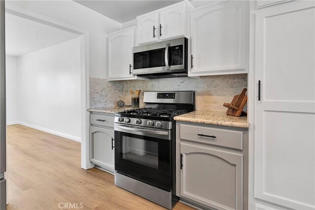 kitchen with tasteful backsplash, white cabinetry, stainless steel appliances, and light wood-type flooring