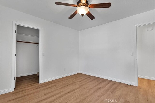 unfurnished bedroom featuring a closet, light hardwood / wood-style flooring, a spacious closet, and ceiling fan