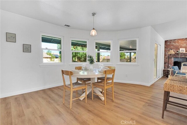 dining room featuring lofted ceiling, light wood-type flooring, and a fireplace