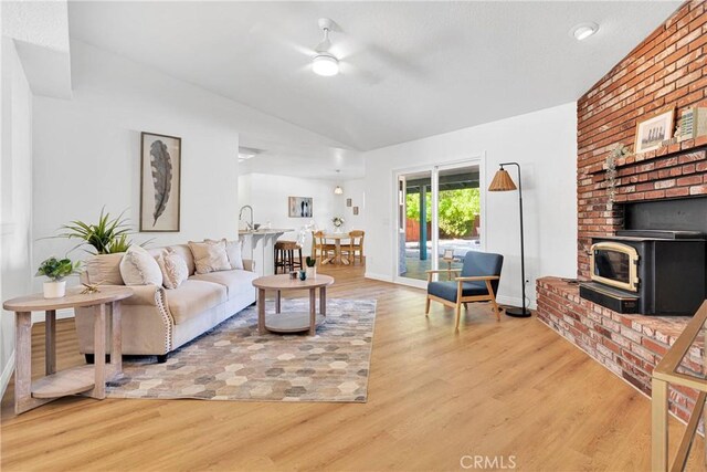 living room featuring a wood stove, ceiling fan, sink, and wood-type flooring